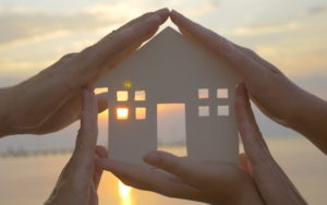 Hands holding cut out house over sunset