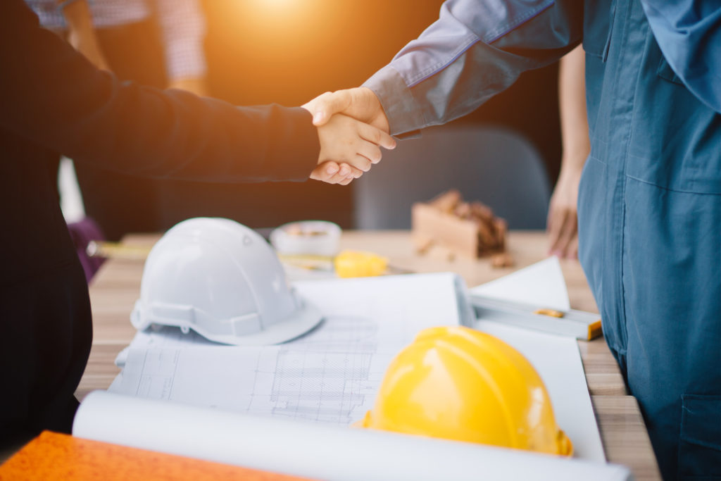 Close-up of a businessman shaking a contractors hand with blueprints on the table