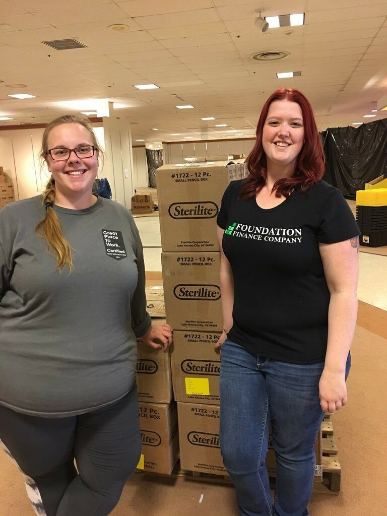 Two Foundation Finance Company employees standing in front of cardboard boxes smiling