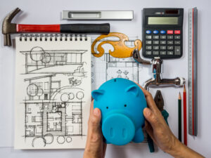 Hands holding piggy bank over architecture drawing with tools surrounding
