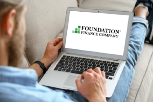 Man sitting on couch looking at his computer with Foundation Finance Company's logo