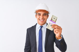 Young handsome architect man wearing helmet holding dollars