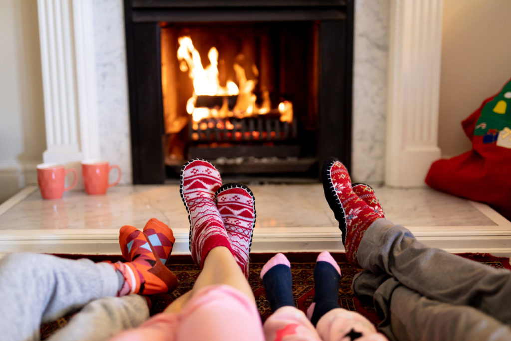 Family lying on the floor, a couple with their young son and daughter warming their feet together in front of a fireplace.