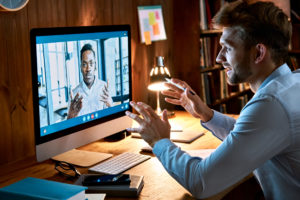 Caucasian business man talking with african male partner coach on video conference call discussing social distance work