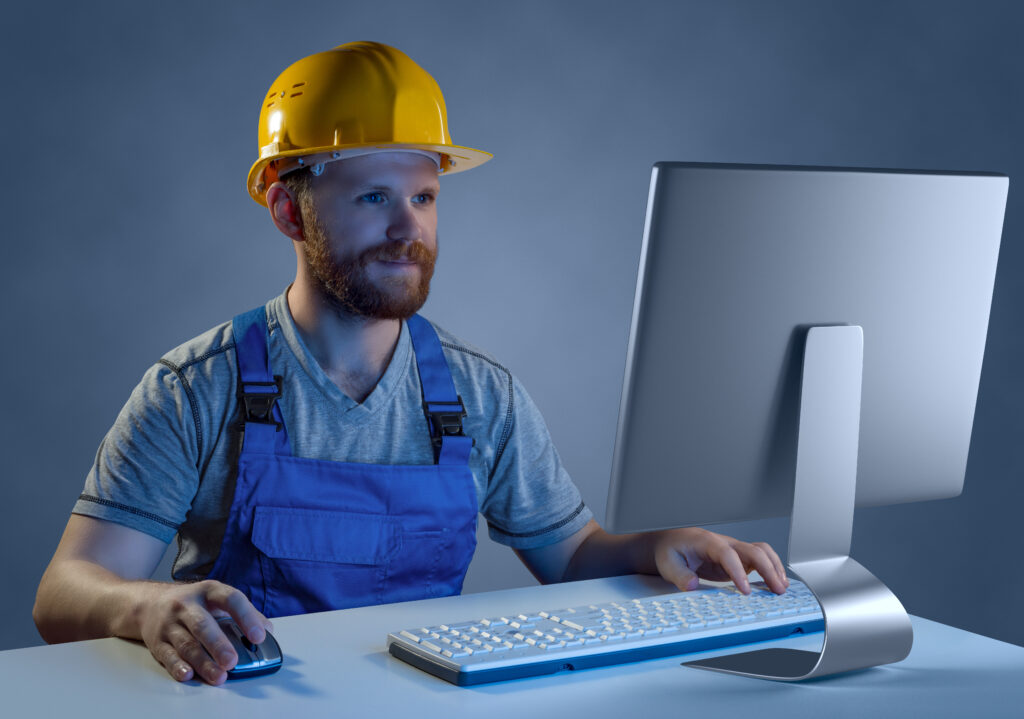 Contractor in work outfit sitting at a desk looking at a desktop computer