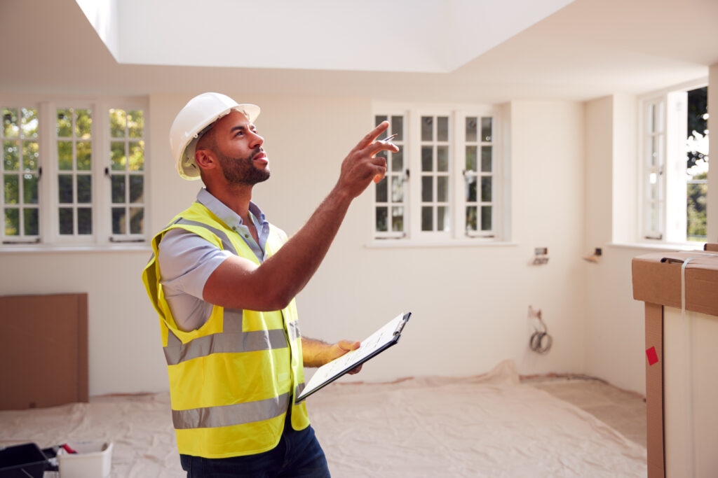 building surveyor wearing hard hat with clipboard looking at interior of new property